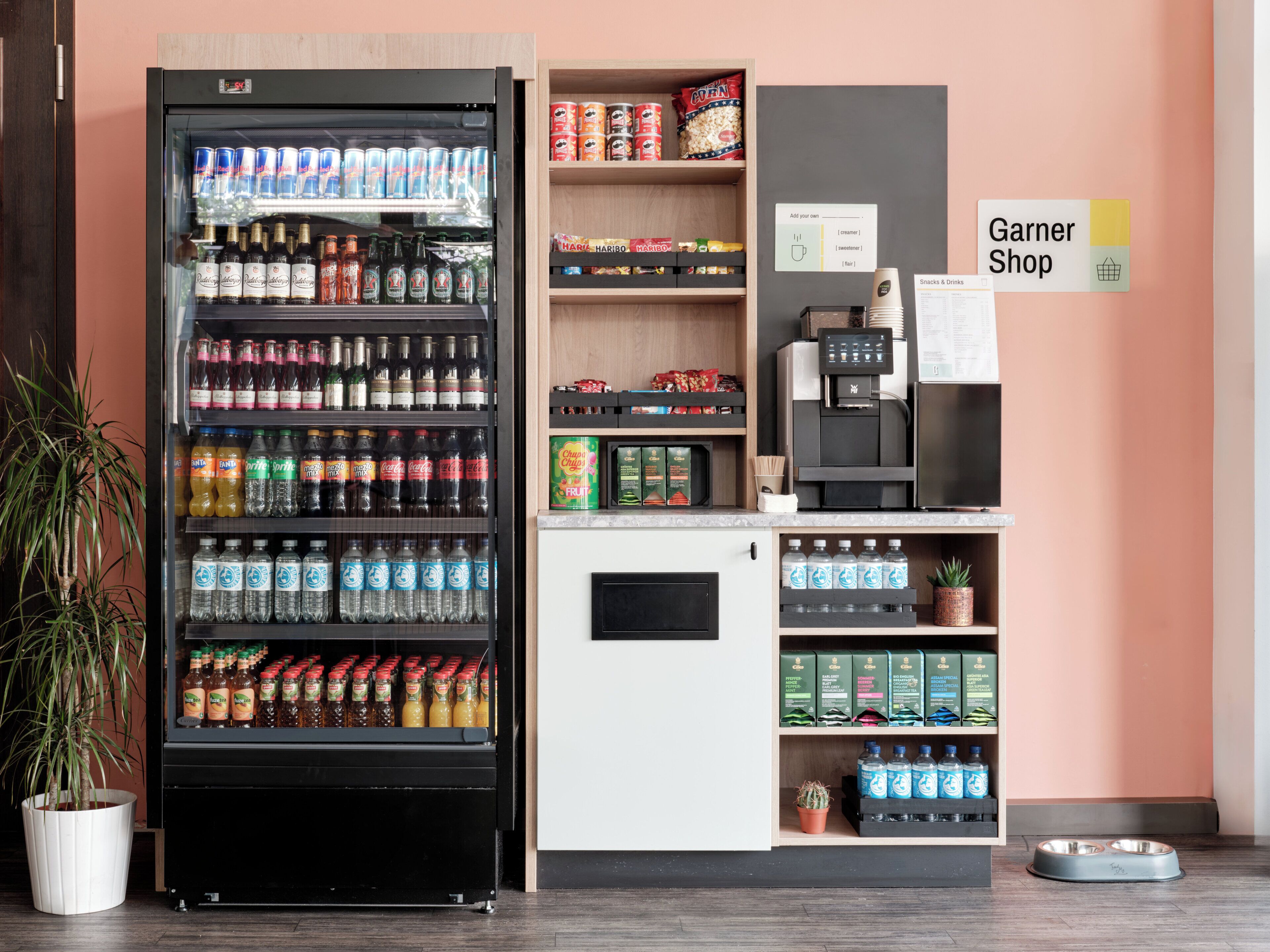 Un distributeur automatique proposant diverses boissons et collations, une machine à café et un petit espace dédié aux animaux de compagnie, avec un bol pour chien.