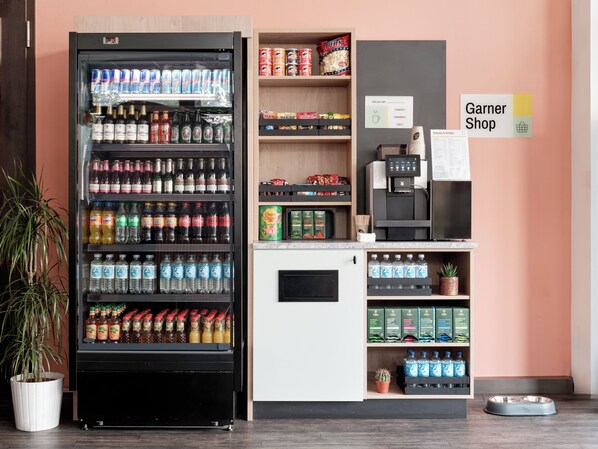 Máquina expendedora con diversas bebidas y aperitivos, máquina de café y una pequeña zona para mascotas con un cuenco para perro.