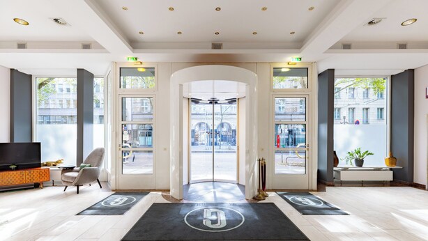 A hotel lobby with a modern design, featuring a reception desk, seating area, and large windows offering views of the street. - Garner Hotel Dusseldorf Main Station by IHG (Düsseldorf)