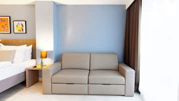 Una habitación de hotel moderna con cama, sofá, mesita de noche con lámpara y cuadros en la pared.