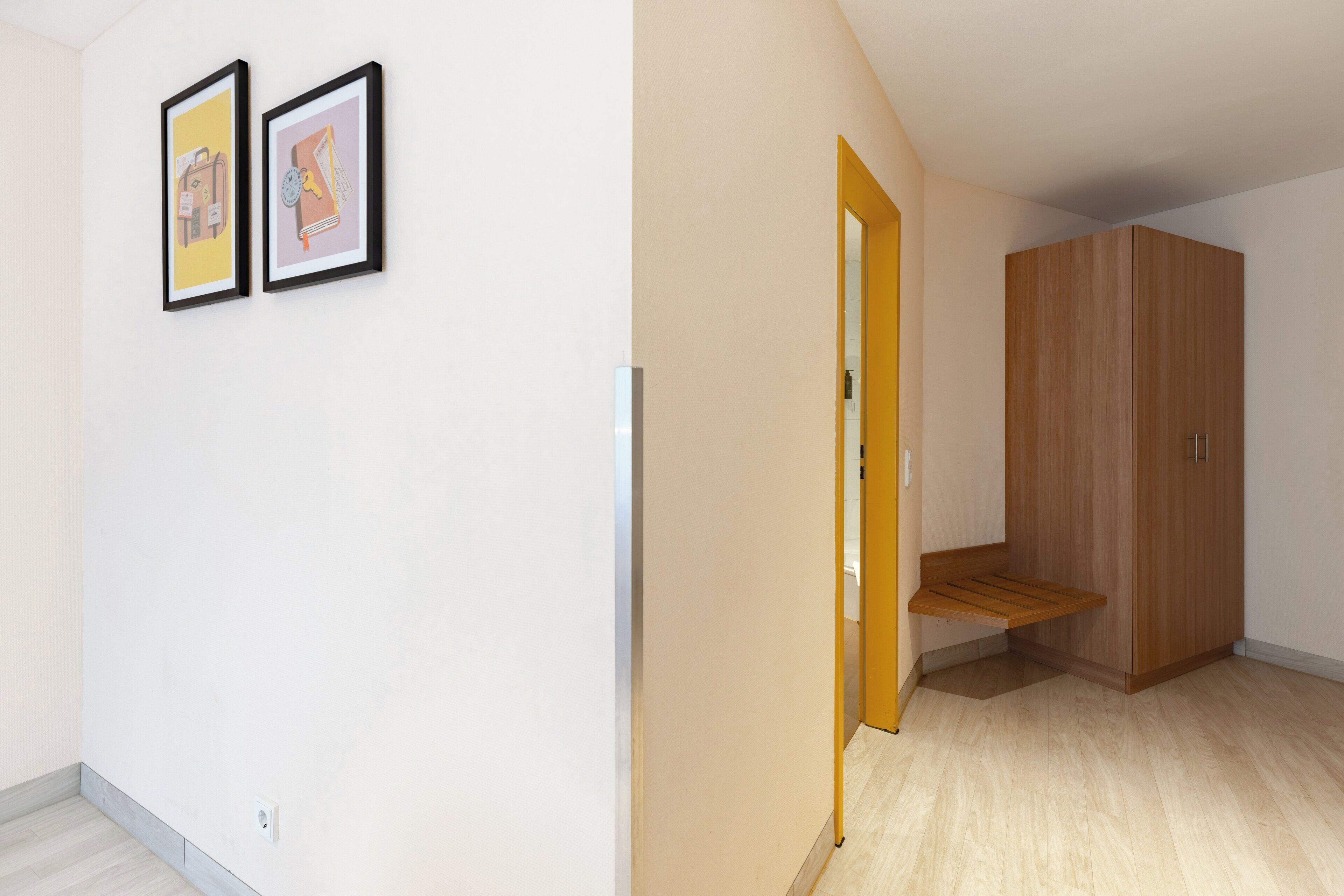 Ein Zimmer mit einem Holzschrank, einer Bank und zwei gerahmten Bildern an der Wand.