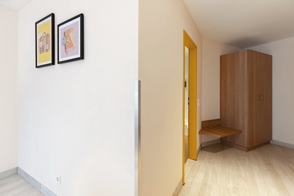 Una habitación con un armario de madera, un banco y dos cuadros en la pared.