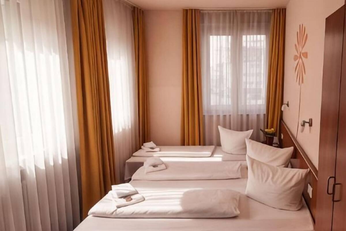 Habitación de hotel con tres camas, un armario y una ventana con cortinas.