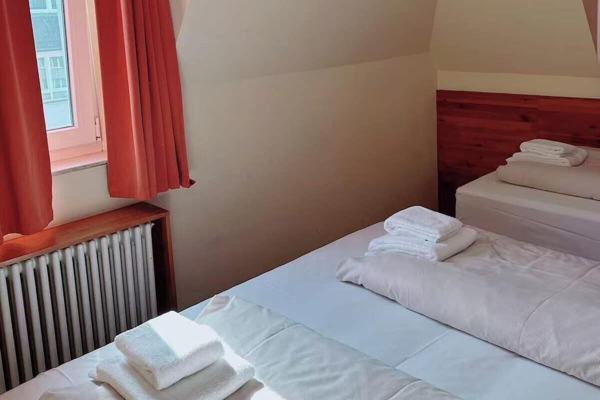 Una habitación con dos camas, una ventana con cortinas rojas y un radiador.