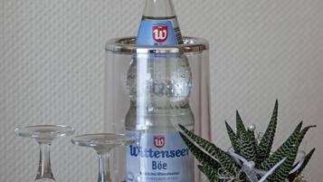 A bottle of Wittsensee mineral water, two empty wine glasses, and a potted succulent plant on a wooden surface.