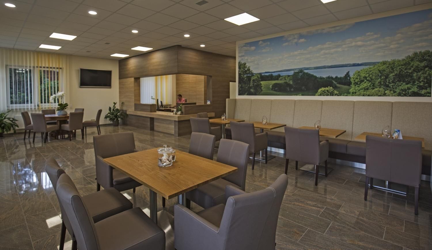 A modern hotel lobby with a reception desk, seating area, and a large scenic mural.