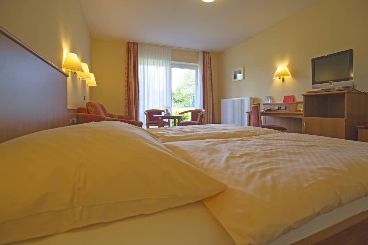 Ein Hotelzimmer mit zwei Betten, einem Schreibtisch, einem Stuhl, einem Fernseher und einem Fenster mit Vorhängen.