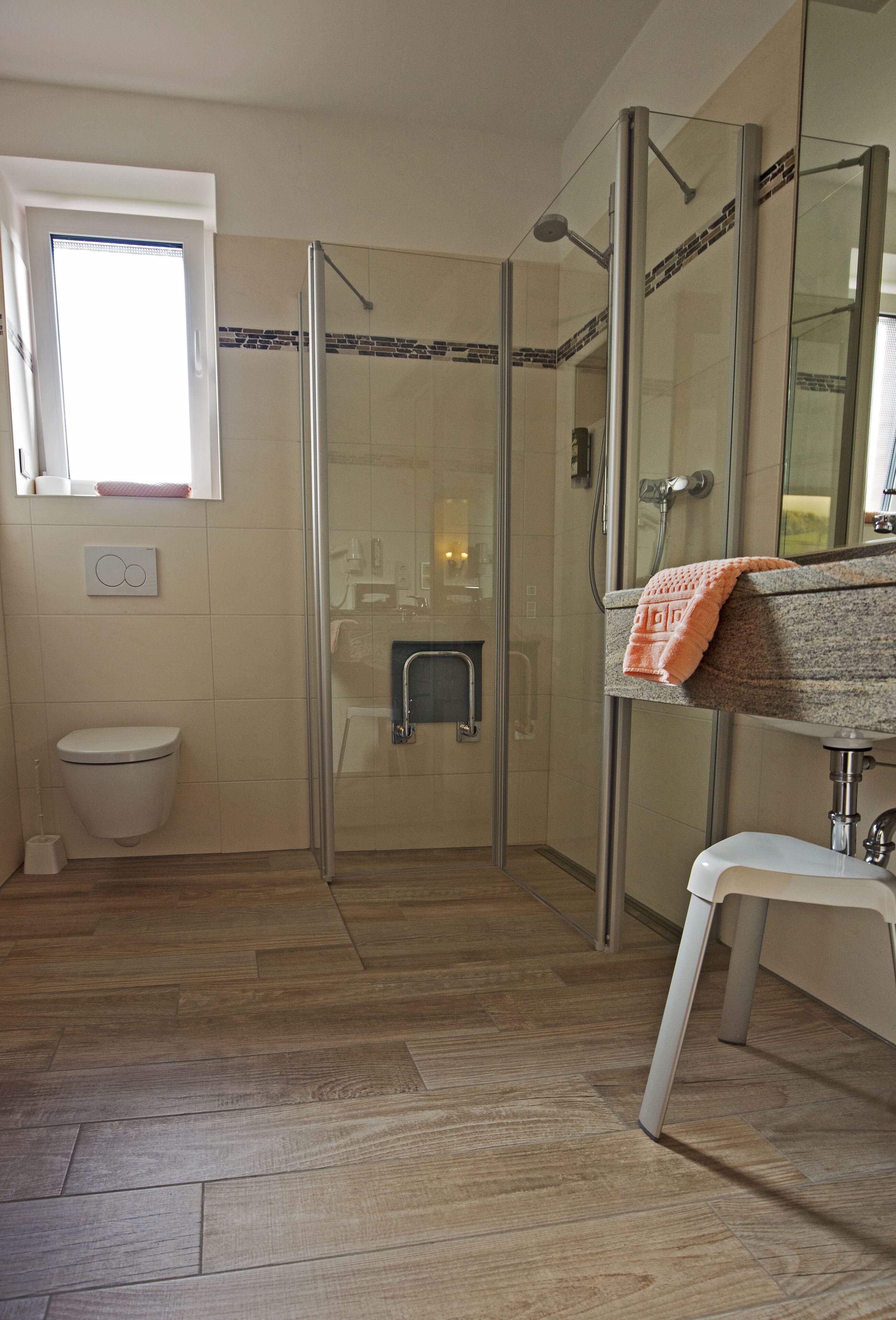 A bathroom with a glass-enclosed shower, a toilet, and a sink with a towel hanging on the wall.