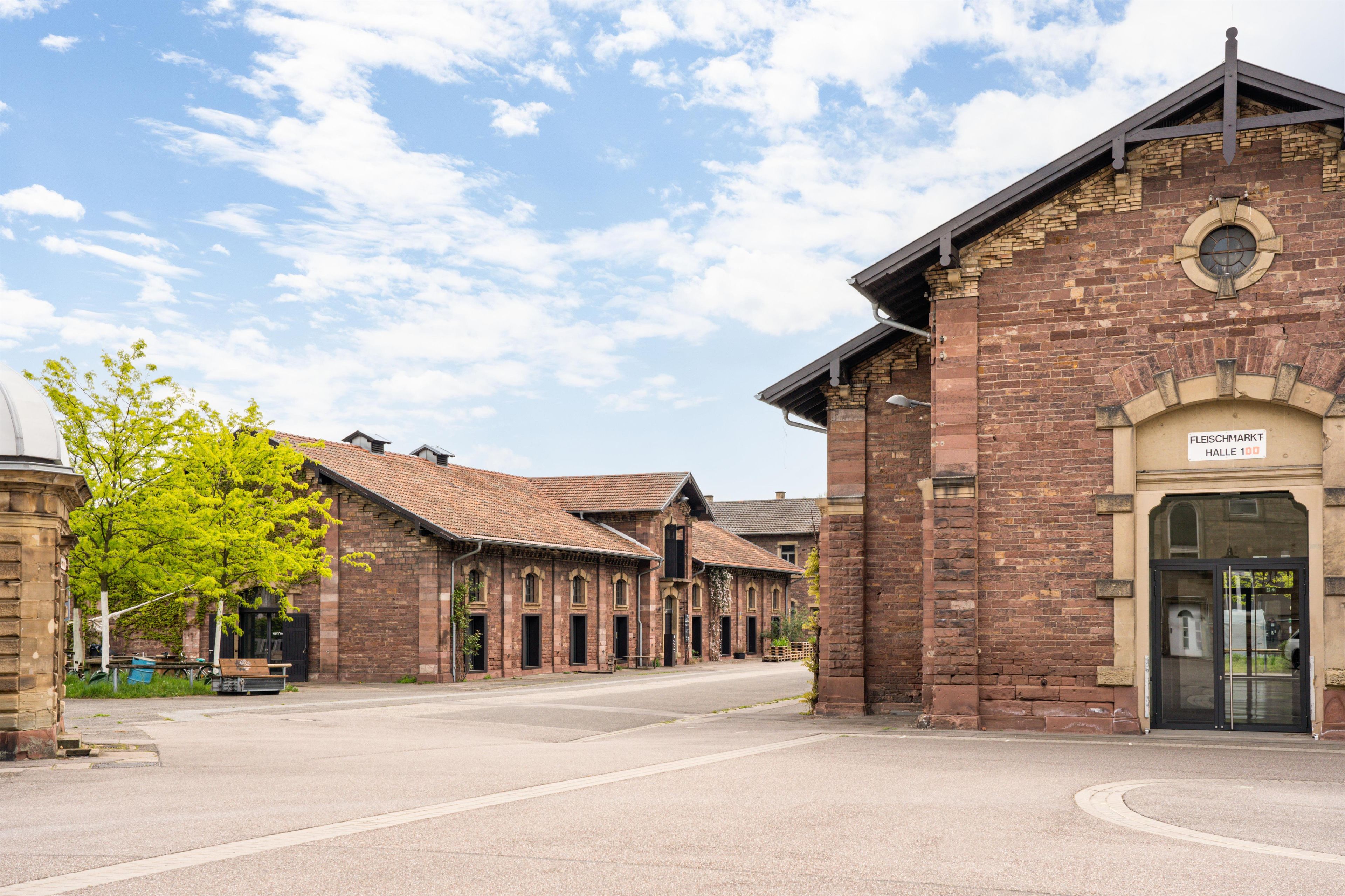 A street with traditional brick buildings, a clear sky, and a sign reading 'FLEISCHMARKT HALLE 100'.