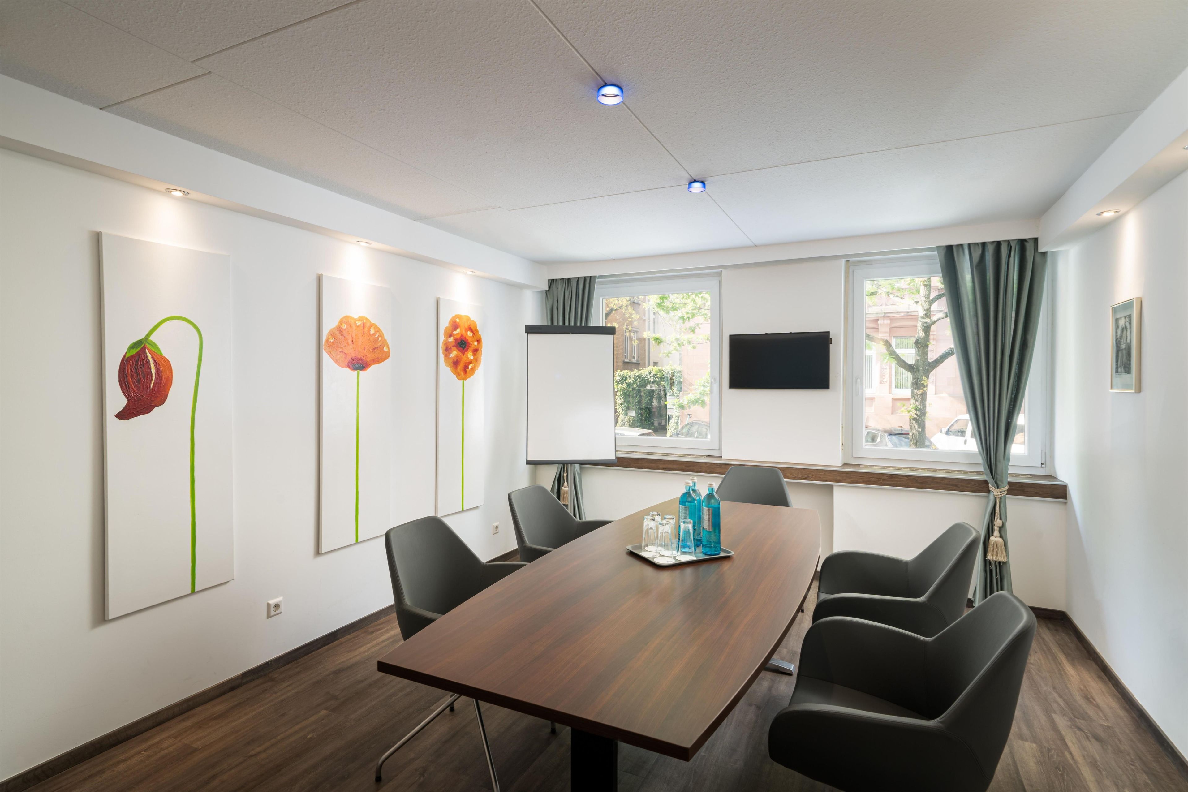 A conference room with a wooden table, black chairs, and artwork on the walls.