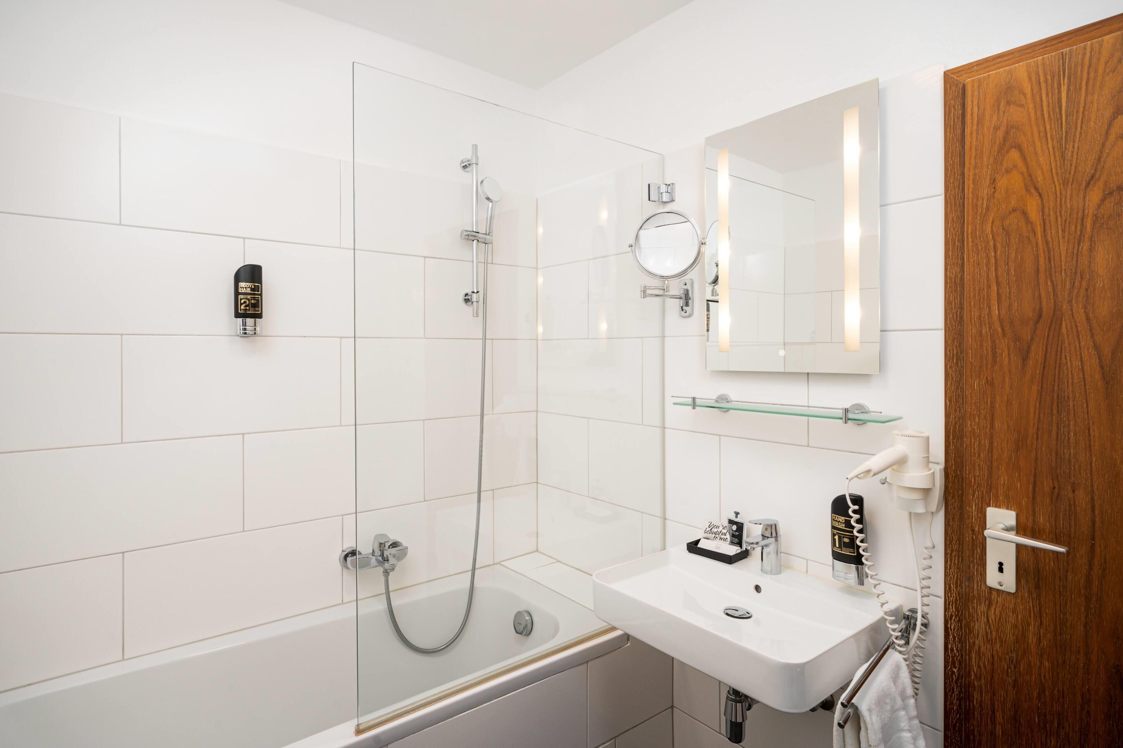 Ein modernes Badezimmer mit Badewanne, Waschbecken, Spiegel und Holztür.