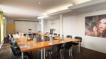 Ein Konferenzraum mit einem langen Tisch, Stühlen und einer Projektionsleinwand.