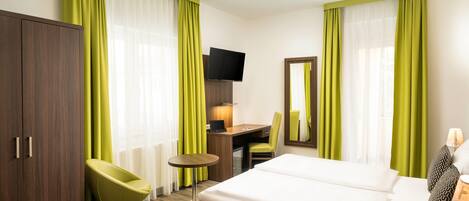 A hotel room with a bed, desk, chair, TV, and wardrobe.