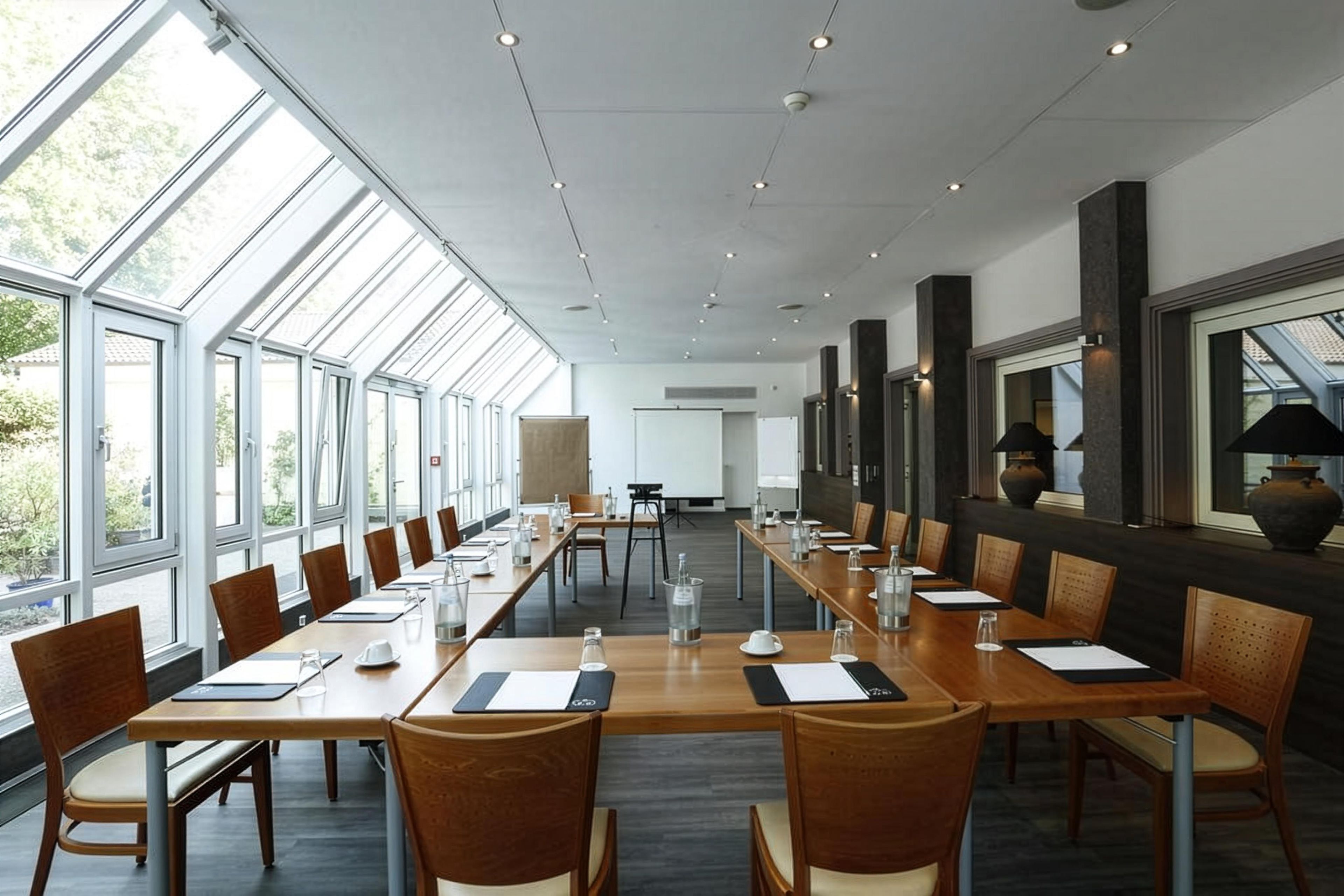 Ein Konferenzraum mit langen Tischen, Stühlen und großen Fenstern.