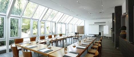 A conference room with long tables, chairs, and a large window providing a view of trees.