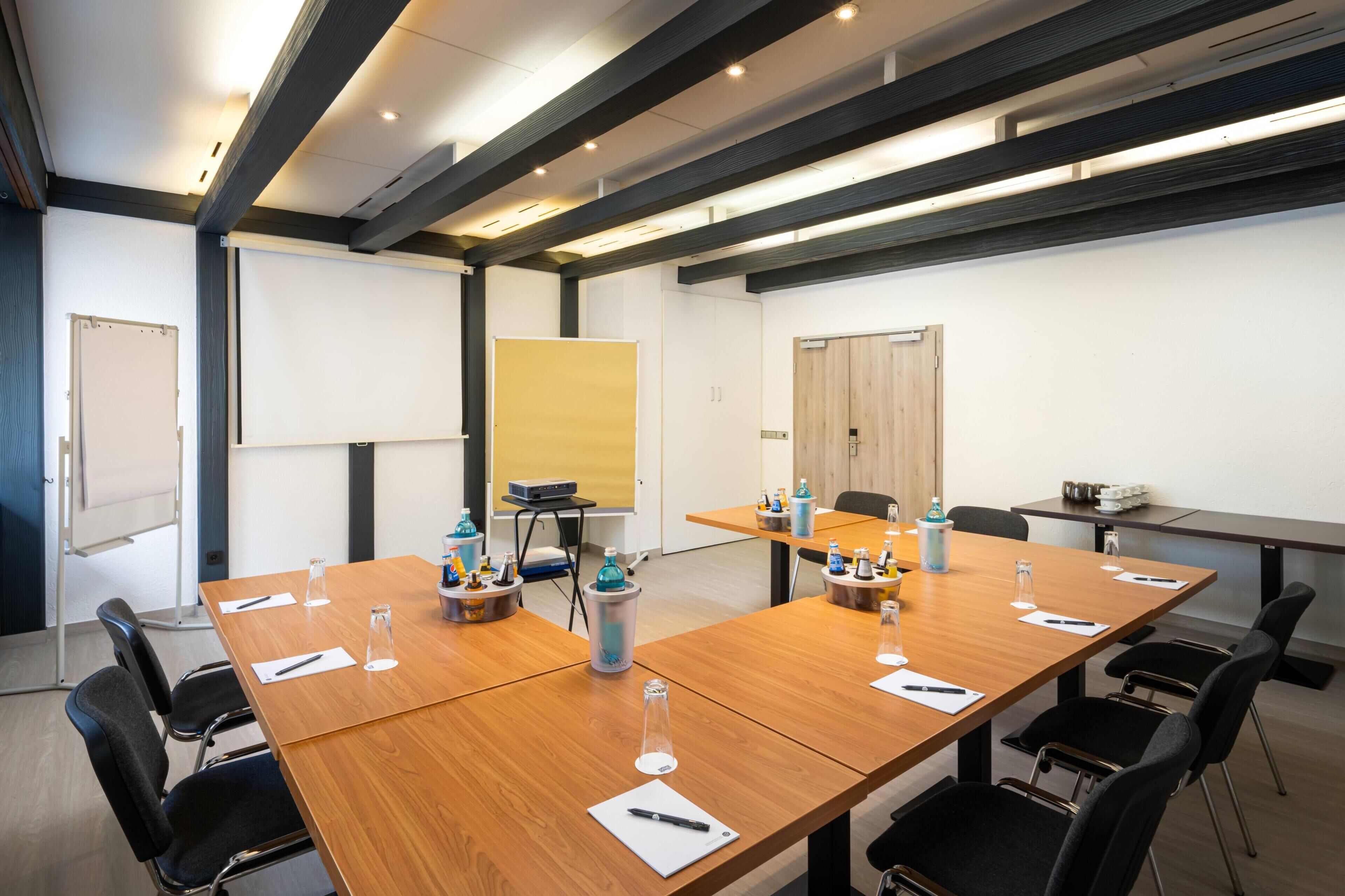 A conference room with long tables, chairs, a whiteboard, and a projector.