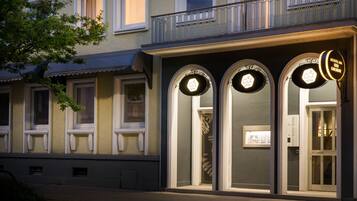 Fachada de hotel con tres letreros iluminados, un balcón y una puerta que dice 'RESTAURANT'.