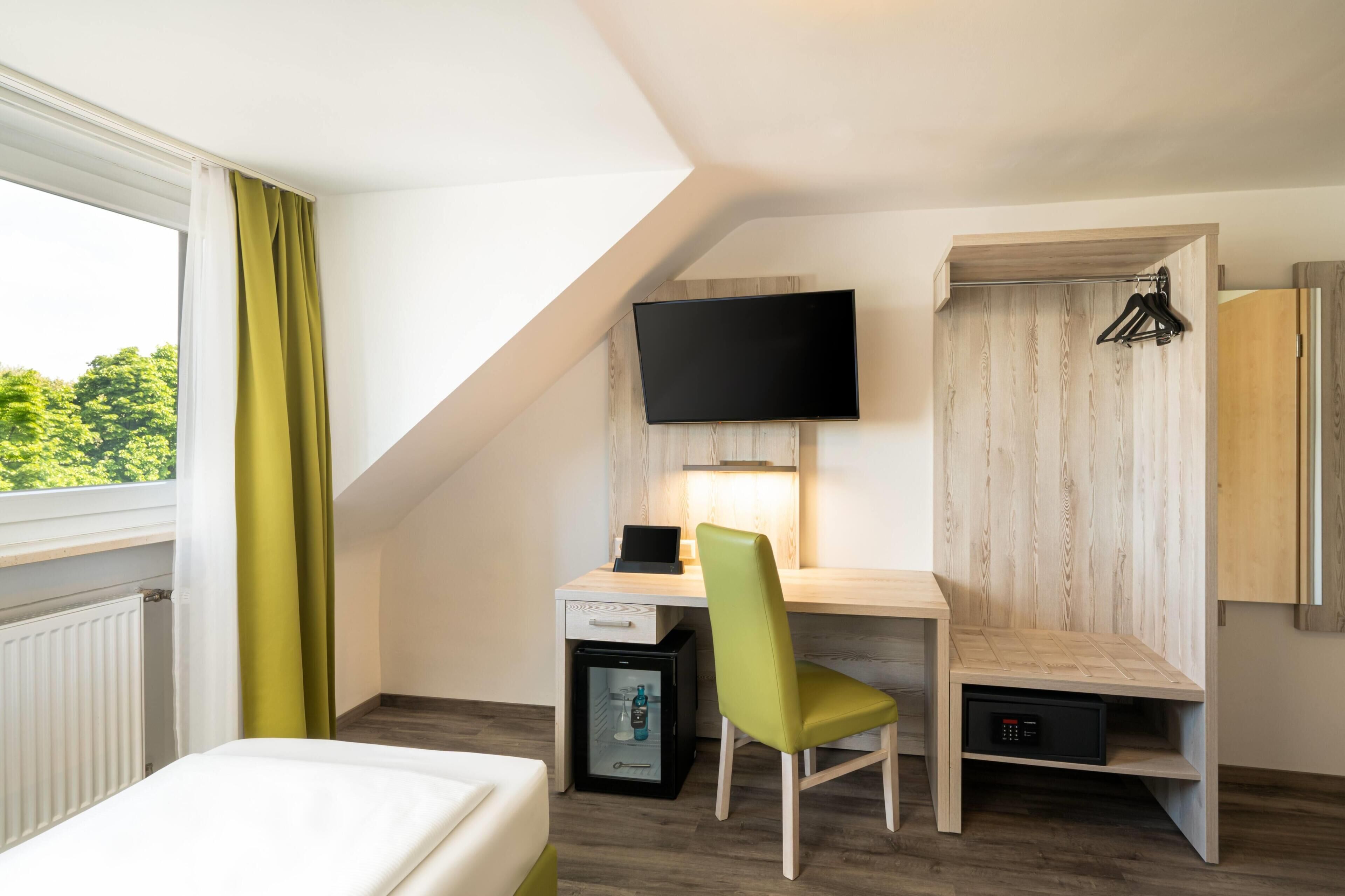 A hotel room with a bed, a desk with a chair, a television, and a wardrobe.