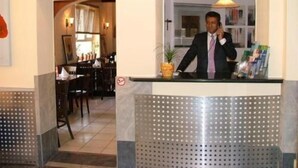 A hotel reception area with a man at the counter, a dining area in the background, and a modern design with perforated panels. - Hotel Aria (Frankfurt)
