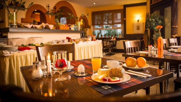 A breakfast setting with a table set for two, featuring a plate of eggs, toast, fruit, and a glass of orange juice. - Hotel Aria (Frankfurt)