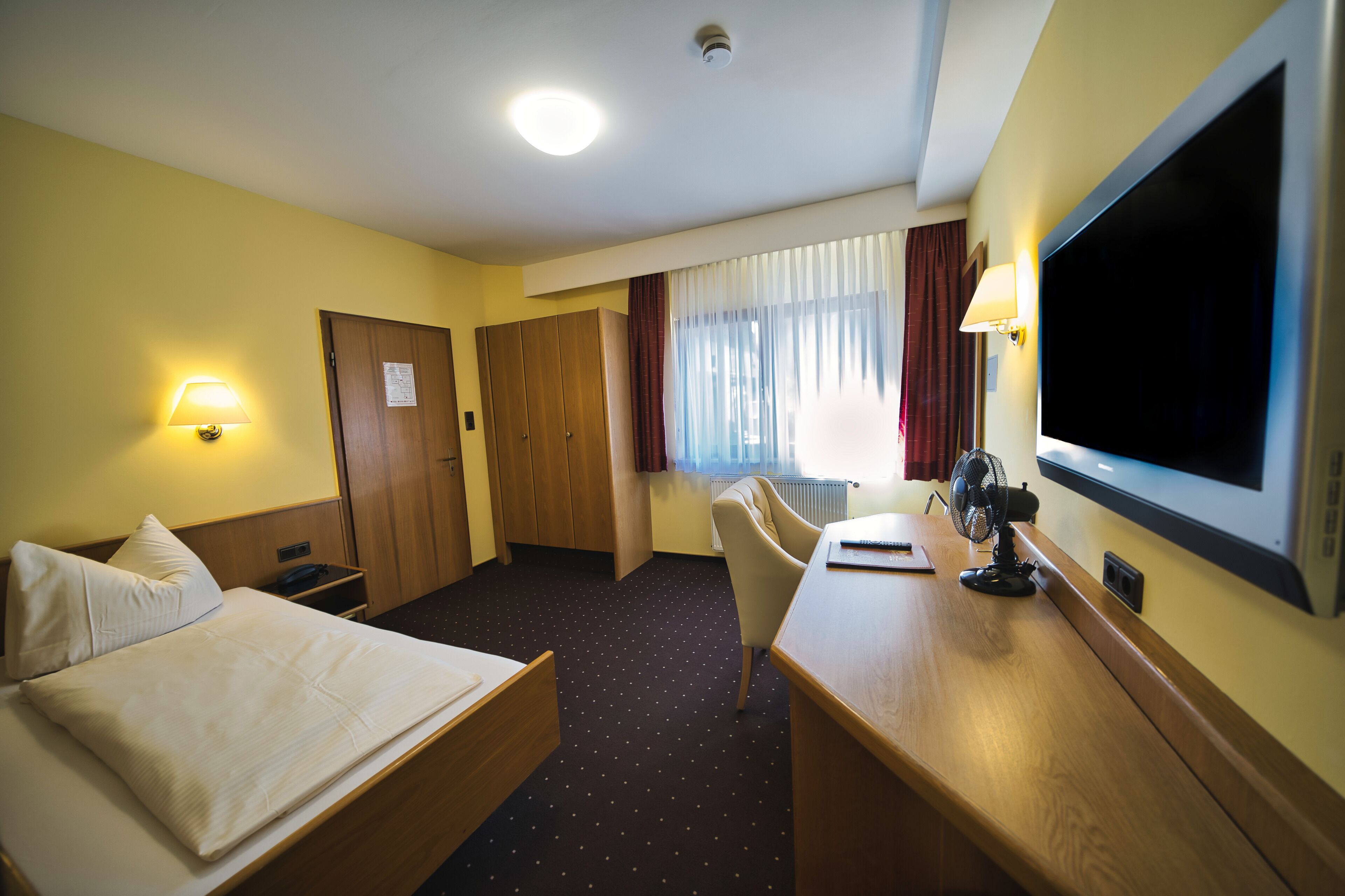 A hotel room with a bed, desk, chair, TV, and a door leading to another room.