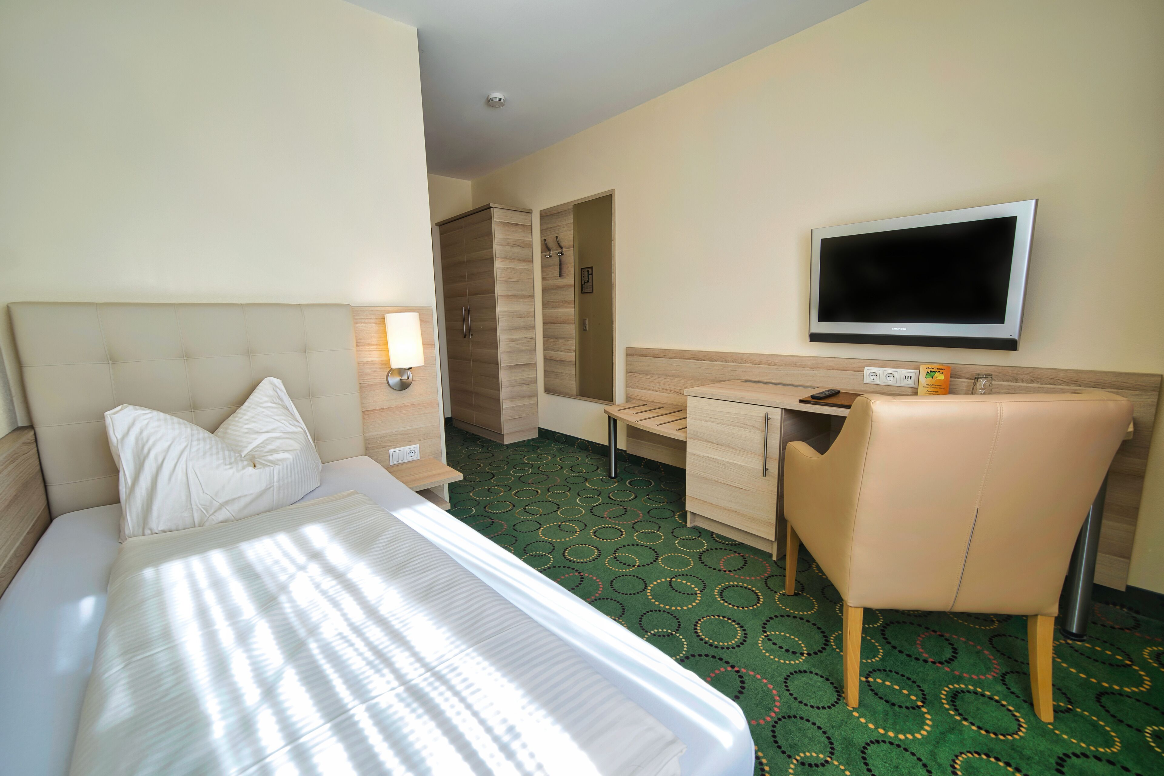 A hotel room with a bed, a desk, a chair, a television, and a wardrobe.