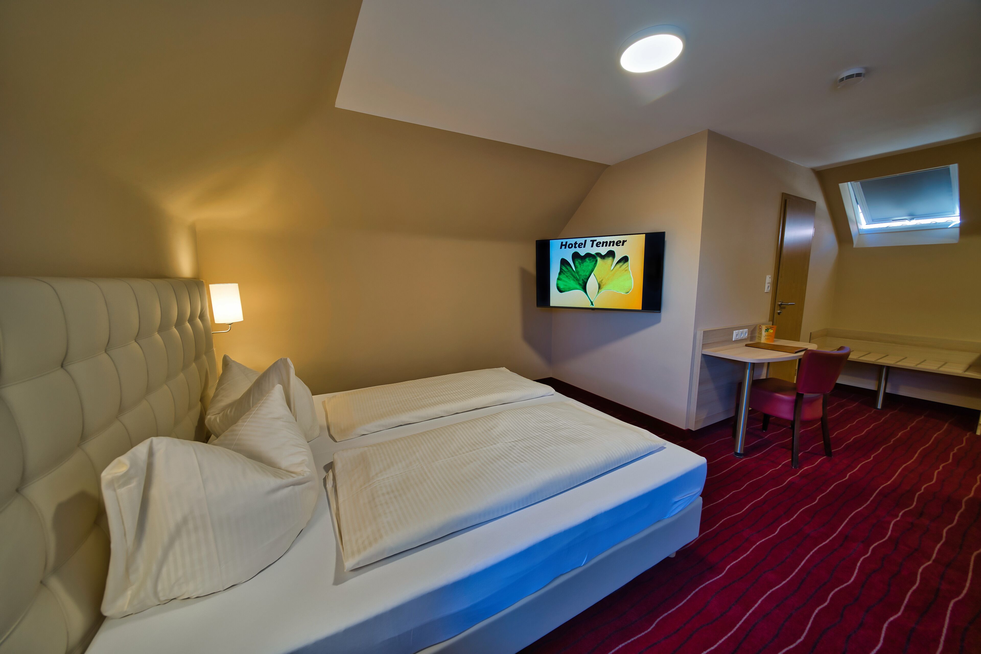 A hotel room with a bed, a desk, a chair, a TV, and a window.