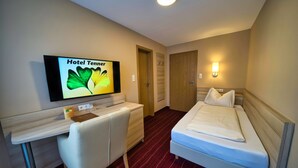 A hotel room with a bed, a desk, a chair, a television displaying 'Hotel Tanner', and a wall-mounted light. - Hotel Tenner (Neustadt an der Weinstrasse)