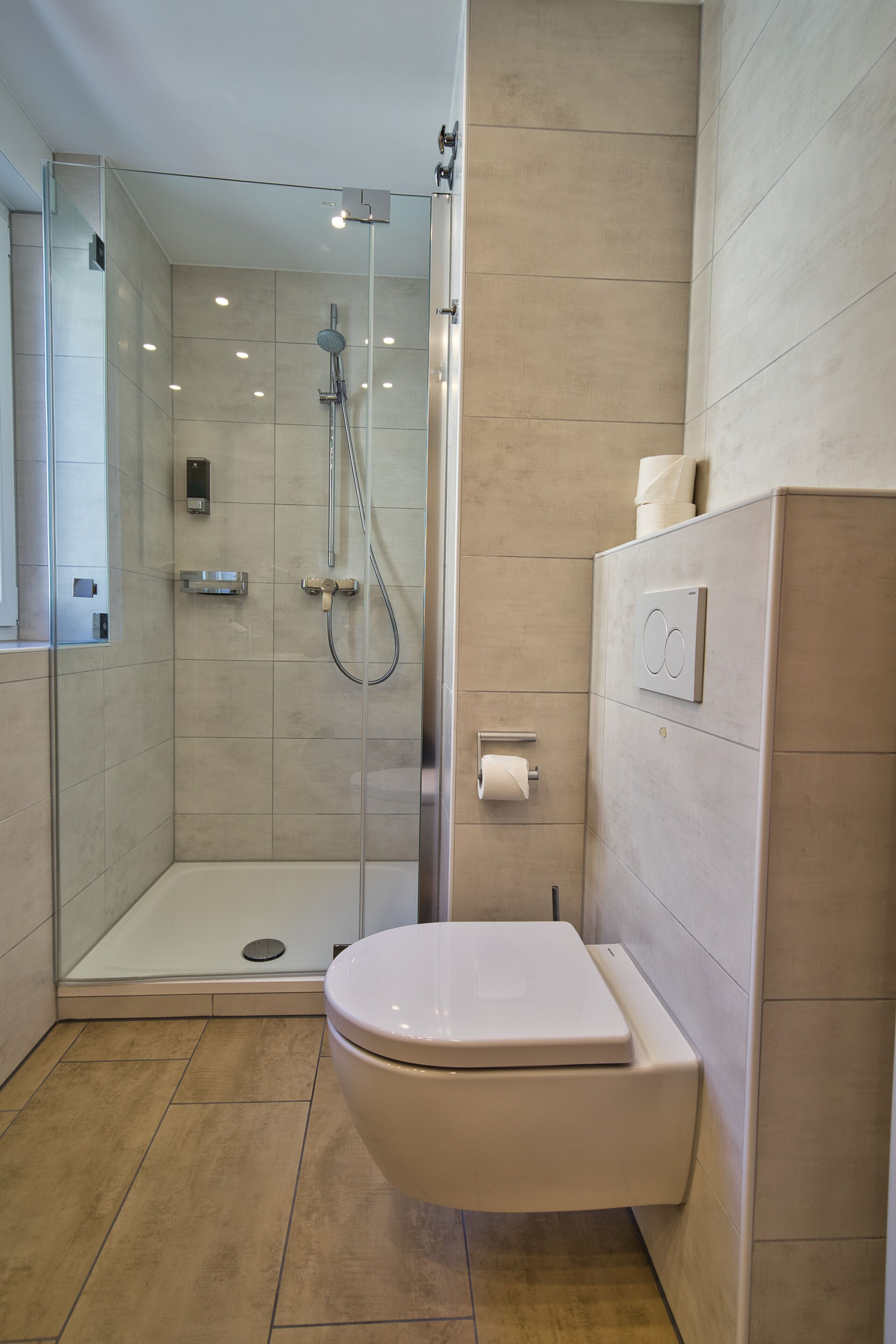 A modern bathroom with a glass-enclosed shower, a white toilet, and a wall-mounted toilet paper holder.
