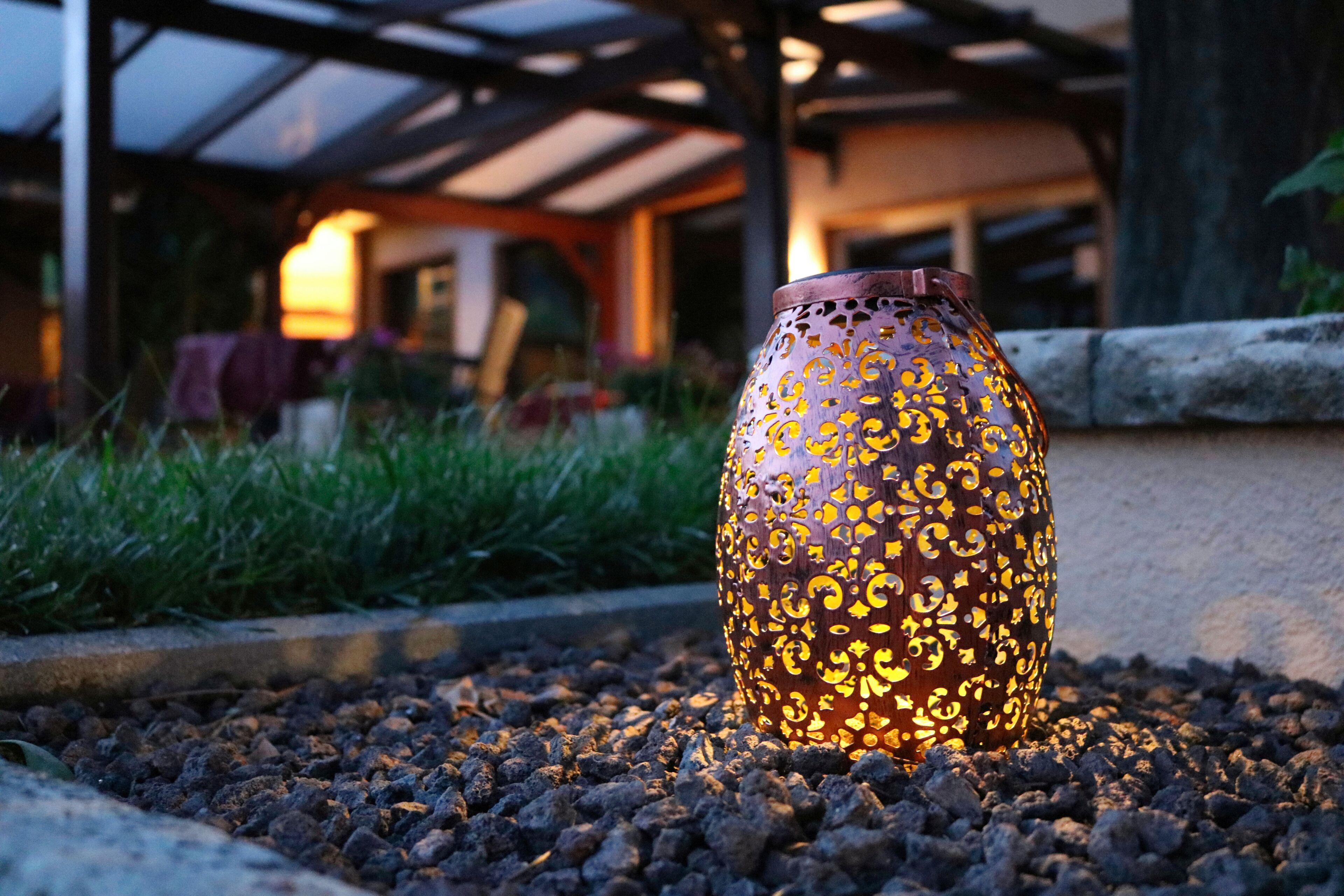 A decorative ceramic vase with intricate patterns, placed on a gravel surface outdoors.
