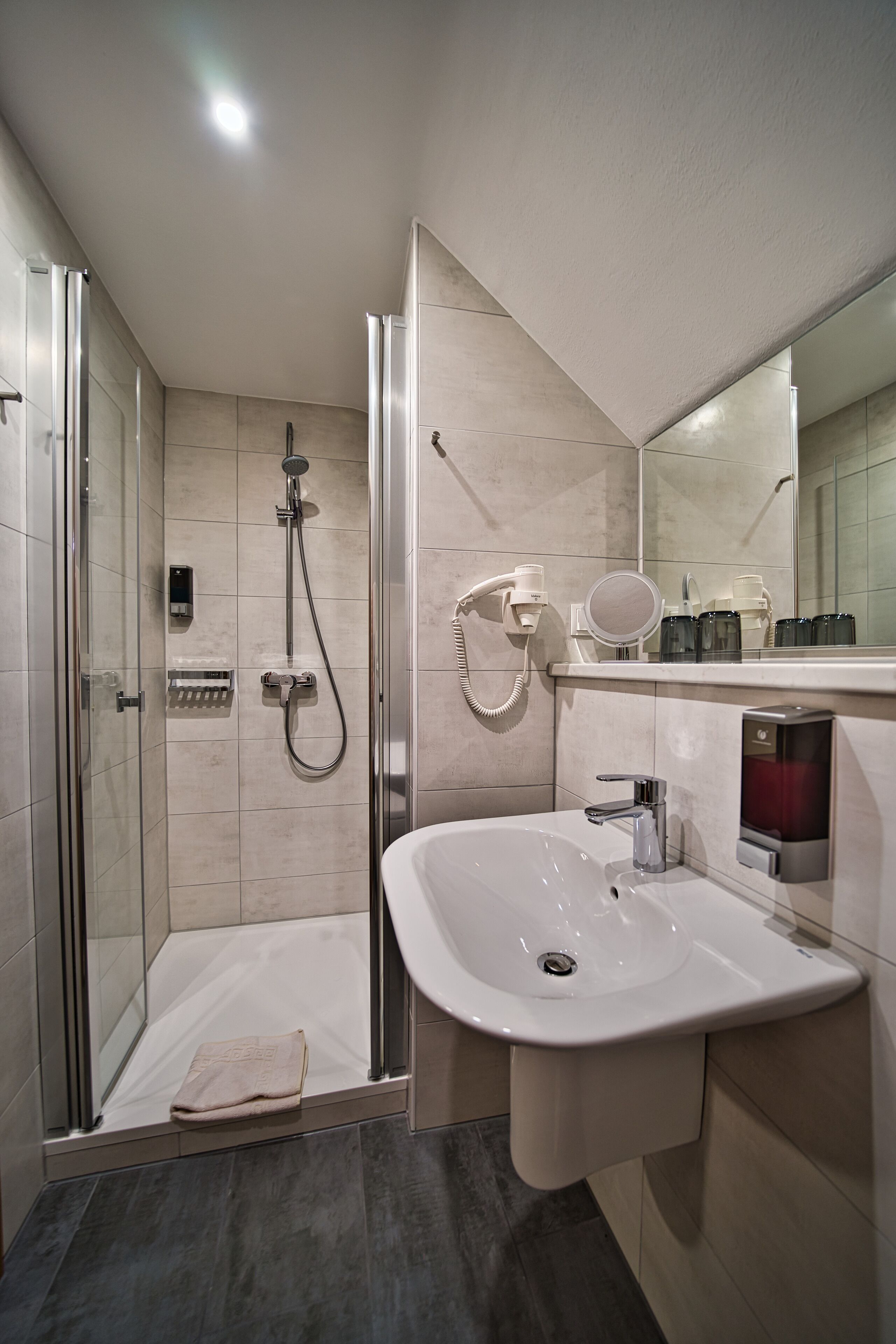 Un baño moderno con ducha envuelta en vidrio, un lavabo blanco y un espejo sobre él.