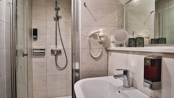 Un baño moderno con ducha envuelta en vidrio, un lavabo blanco y un espejo sobre él.