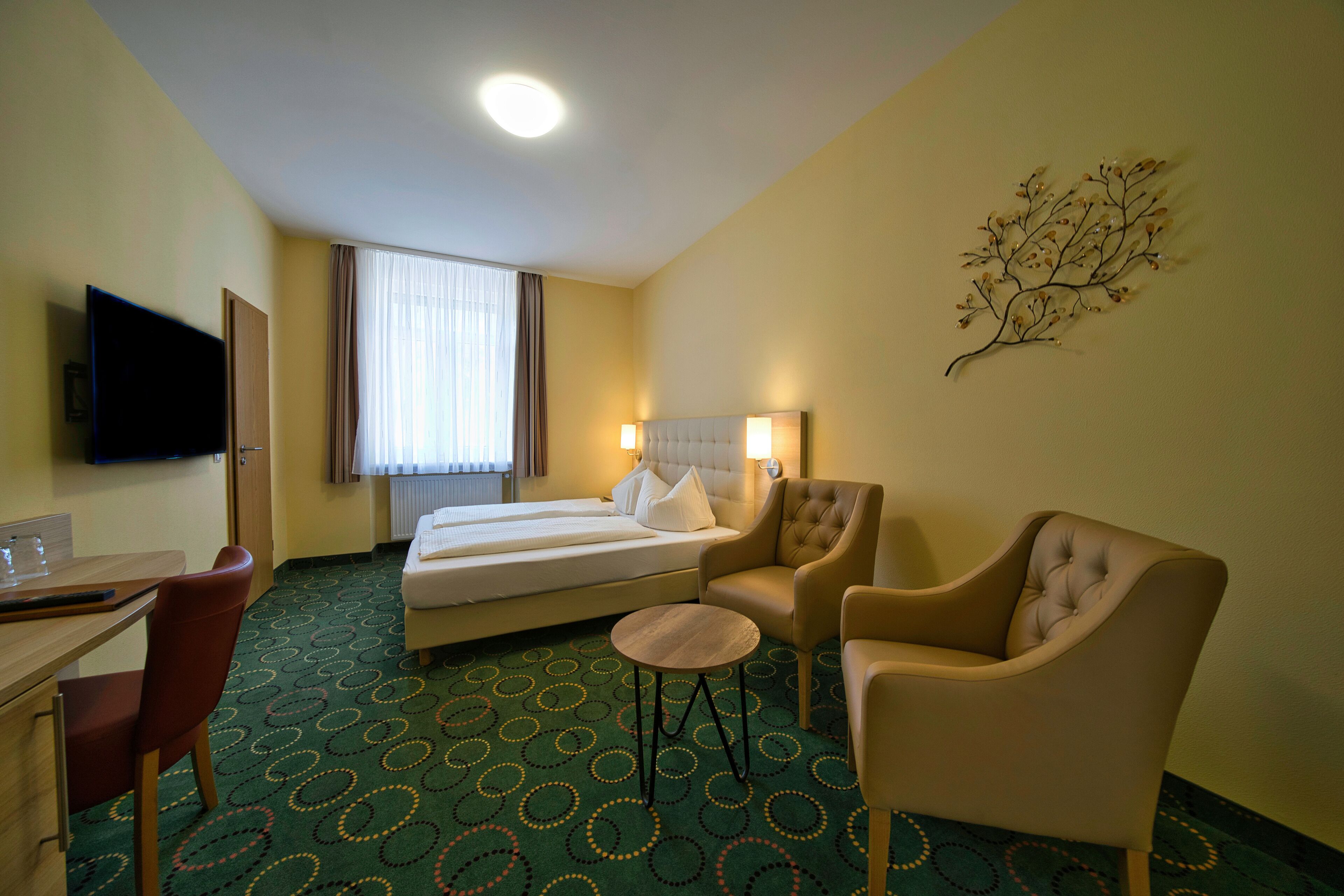 Habitación de hotel con una cama, dos sillones, una mesita, un televisor y una ventana con cortinas.