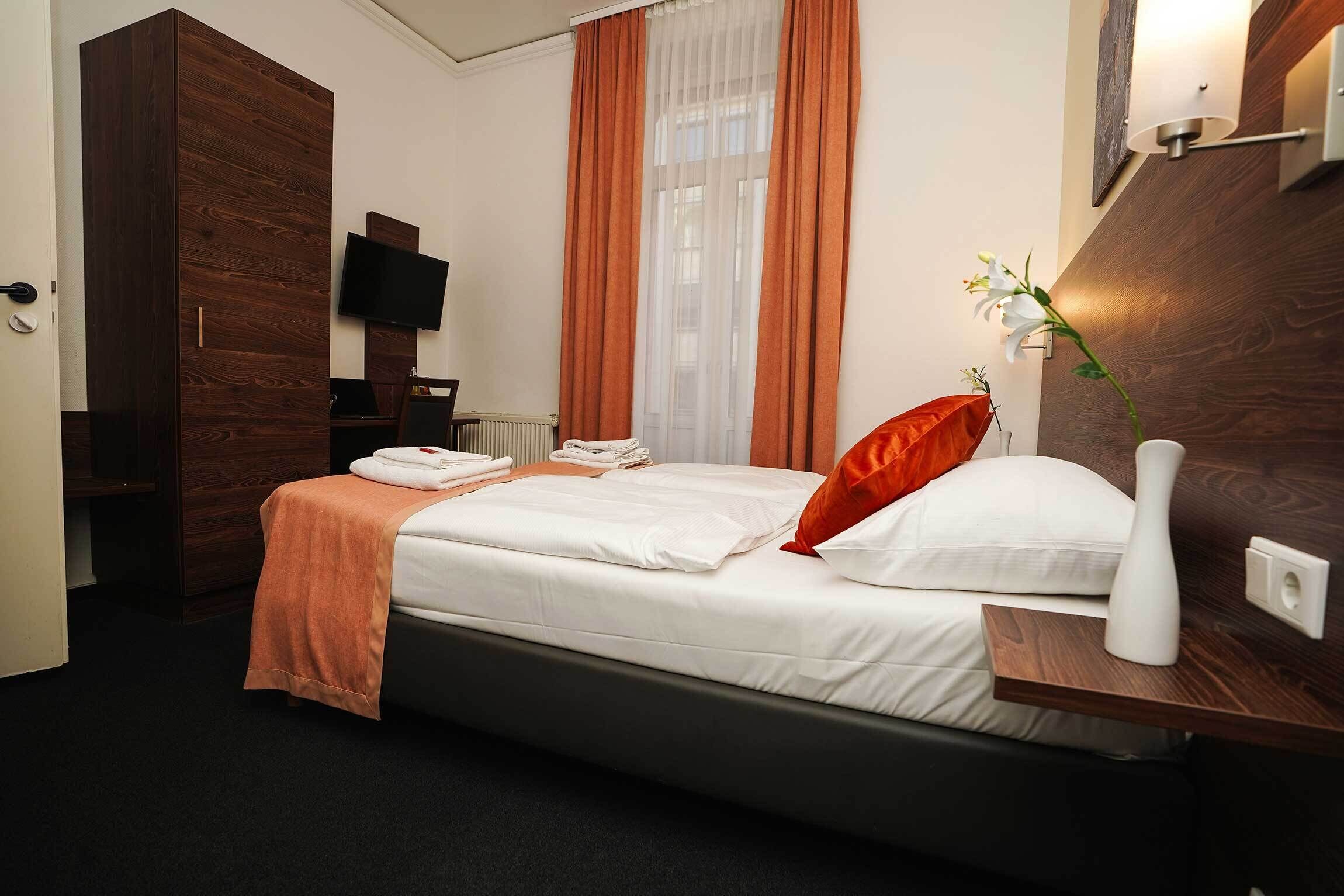 Een hotelkamer met een bed, een televisie, een raam met gordijnen, een nachtkastje en een houten kledingkast.