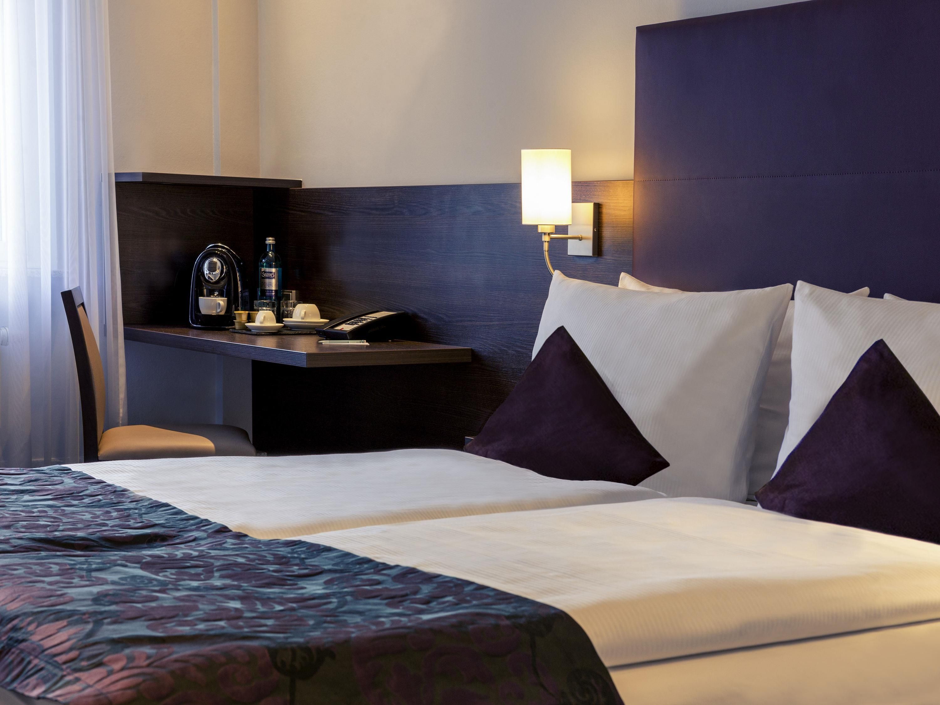 Habitación de hotel con cama, escritorio con lámpara, silla y minibar.