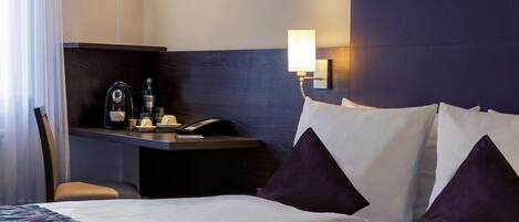 Habitación de hotel con cama, escritorio con lámpara, silla y minibar.