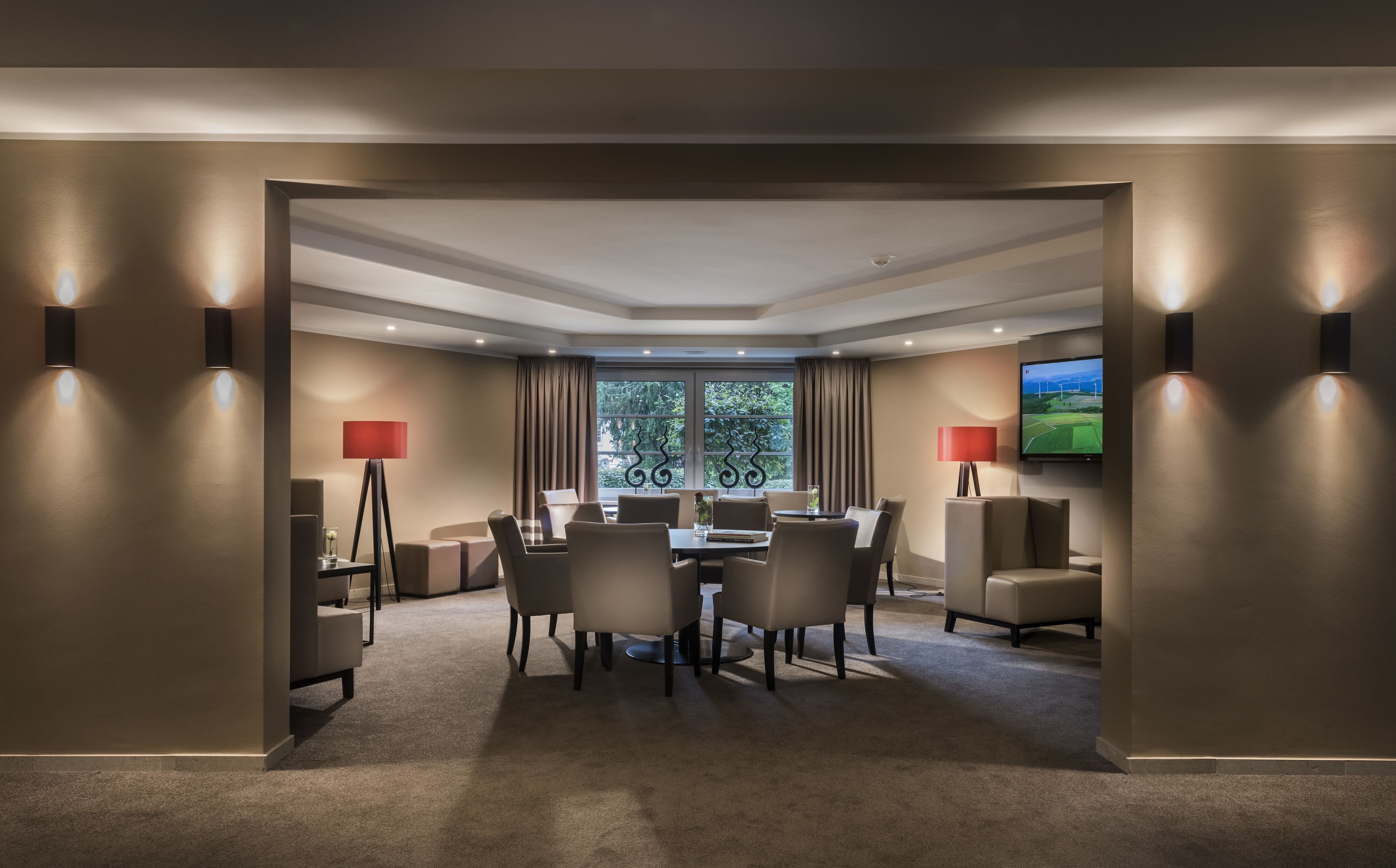 A hotel room with a dining area, a TV mounted on the wall, and a view of trees through the window.