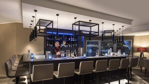 A modern bar area with a long counter, multiple bar stools, and a well-stocked shelf with various bottles. - relexa hotel Harz-Wald (Braunlage)