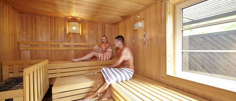 A sauna with wooden benches, a visible heater, and a window with a view of the outside.
