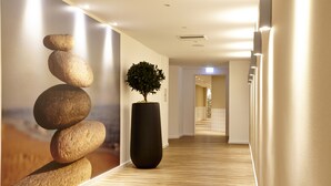 A hallway with a wooden floor, a large potted plant, and a wall-mounted sculpture of stacked stones. - relexa hotel Harz-Wald (Braunlage)