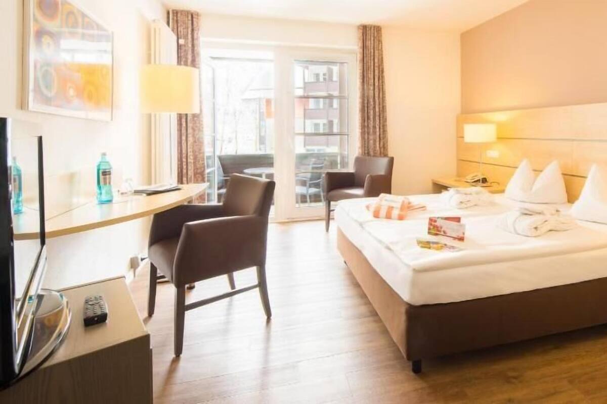 Ein Hotelzimmer mit Bett, Schreibtisch, Stuhl, Fernseher und Blick ins Freie.
