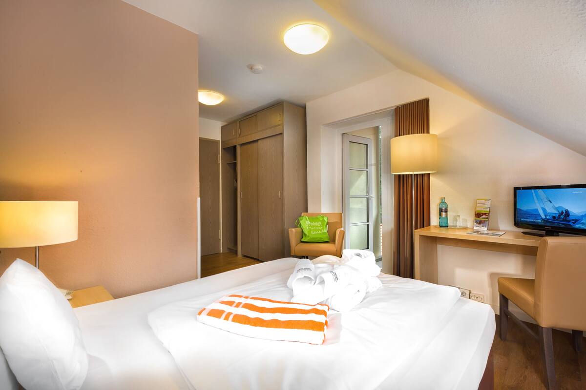 Ein Hotelzimmer mit Bett, Schreibtisch, Stuhl, Fernseher und einem durchgegangenen Tür sichtbaren Badezimmer.