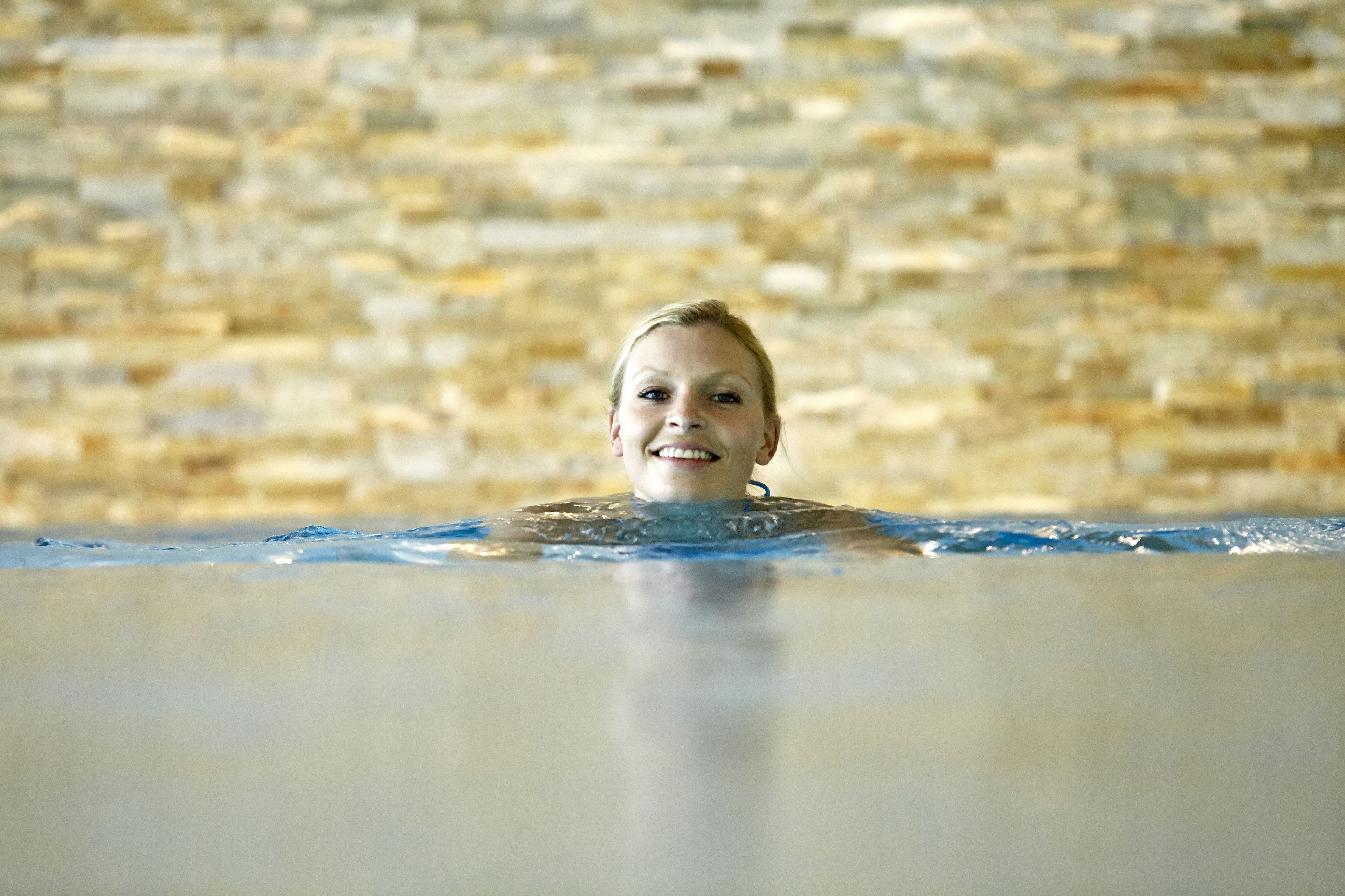 A person in a swimming pool with a stone wall in the background.