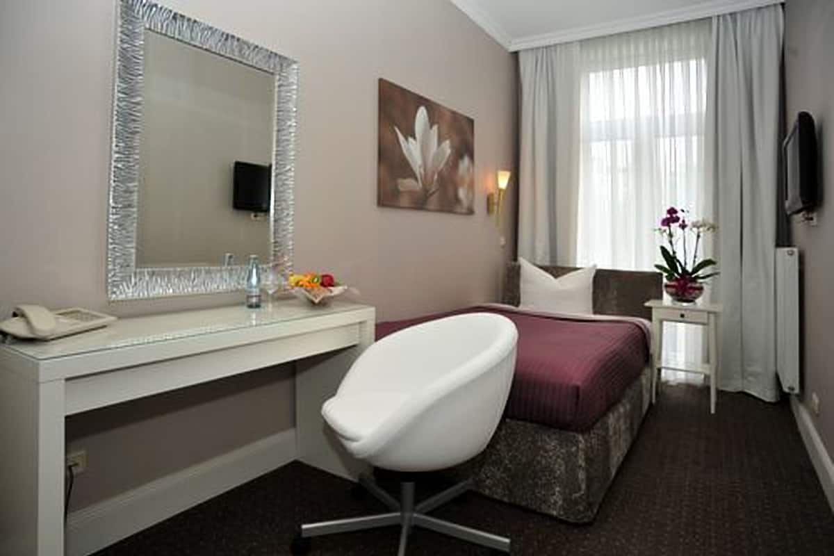 Ein Hotelzimmer mit Bett, Schreibtisch mit Telefon, Stuhl, Nachttisch mit Blumenvase und einem großen Spiegel.