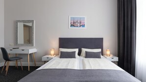 Habitación de hotel con cama, mesitas de noche, escritorio, silla, espejo y un cuadro en la pared.