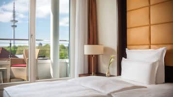 Quarto de hotel com cama, mesa de cabeceira com abajur, um vaso com flores e vista para uma torre através de uma porta de correr.