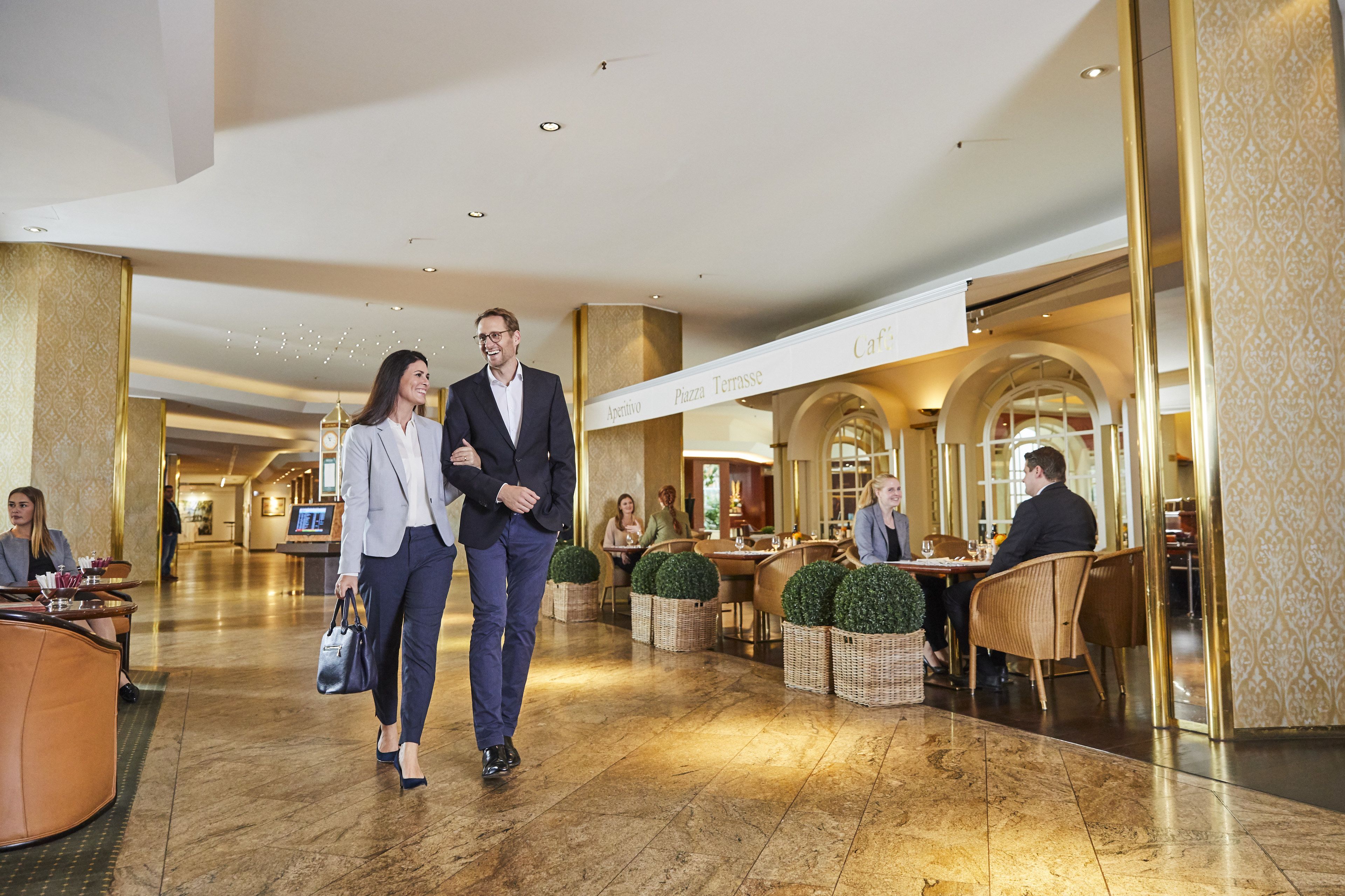 Eine Hotelhalle mit Marmorboden, einer Rezeption und mehreren Essbereichen mit Korbstühlen und Tischen.