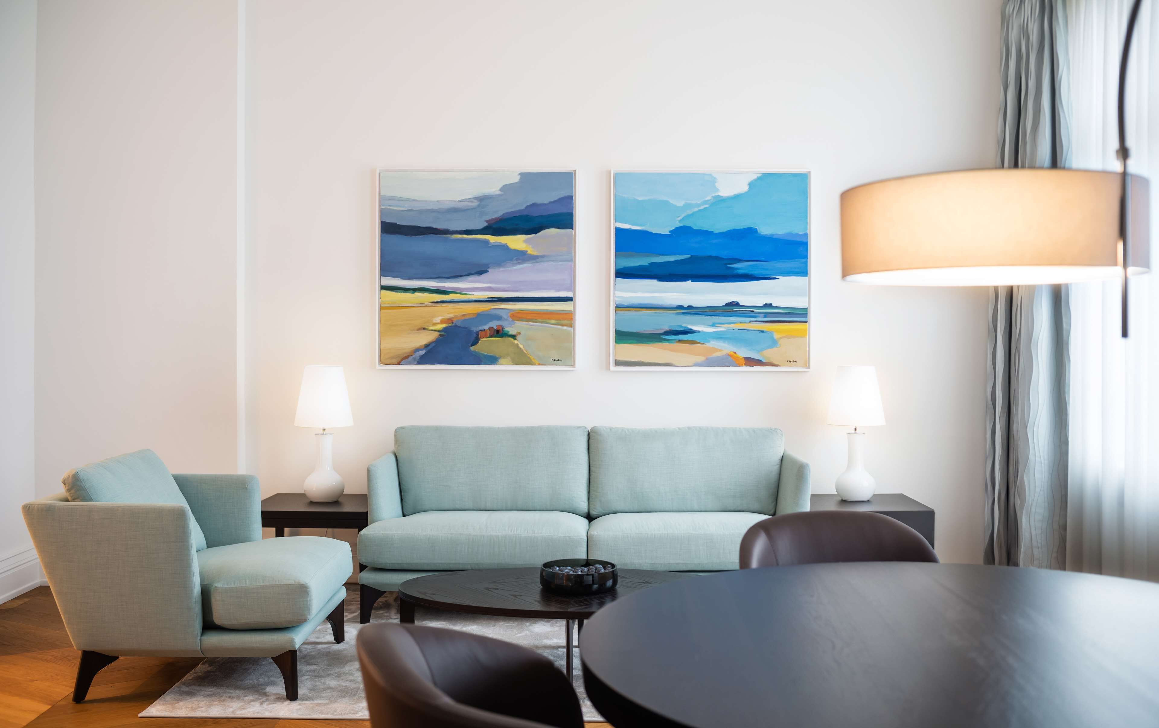 A modern living room with a light blue sofa, a round table, and two paintings on the wall.