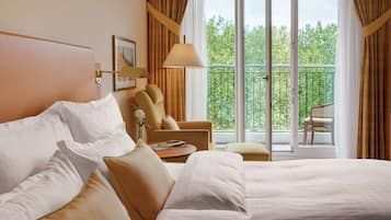 A hotel room with a large bed, a chair, a table, and a view of the outdoors through a balcony.