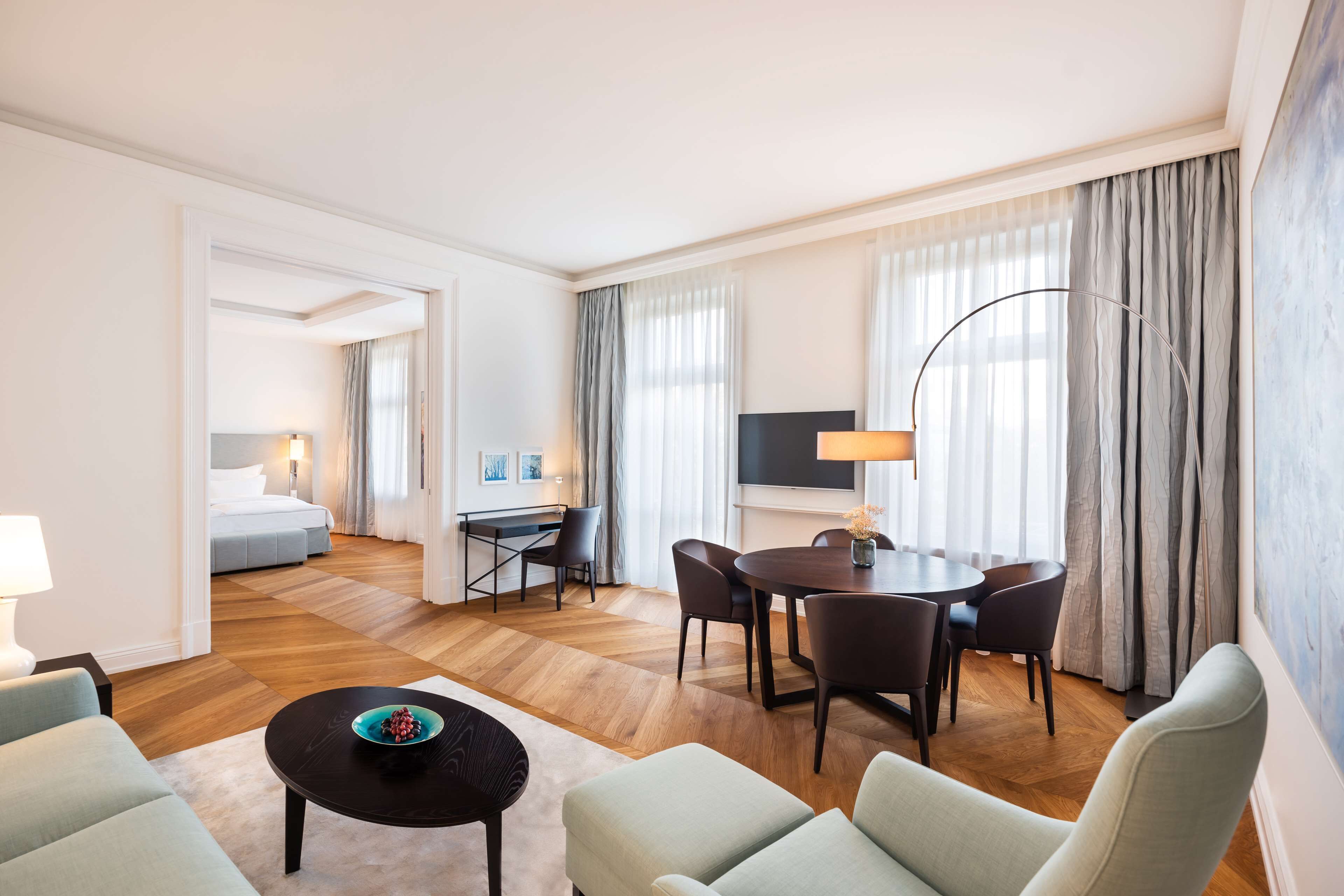 A hotel room with a living area, a dining table, and a TV.